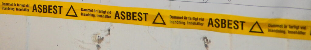 Gul tejp med svart text. ASBEST. damm är farligt att inandas.