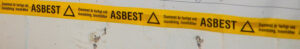 Gul tejp med svart text. ASBEST. damm är farligt att inandas.
