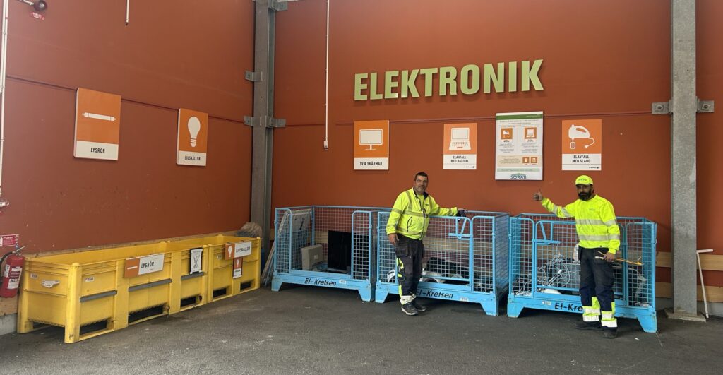 Två varselklädd personal står framför Elektronik på Vallentuna Returpark och visar den nya uppdelningen